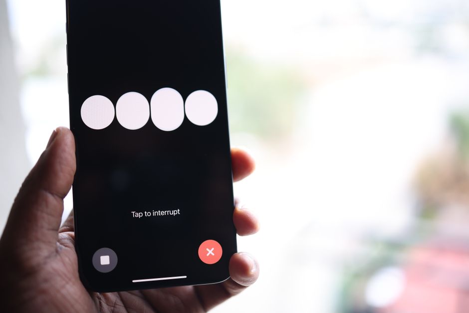 Close-up of a smartphone screen displaying a 'Tap to interrupt' prompt held in a hand.